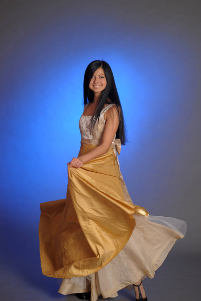 brunette girl in a long golden dress in the studio - Zdjęcie, obraz