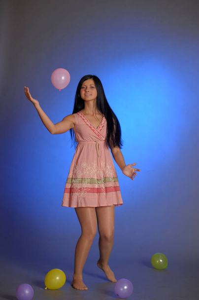 brunette girl in a short pink dress with balloons plays on a blu - Fotoğraf, Görsel