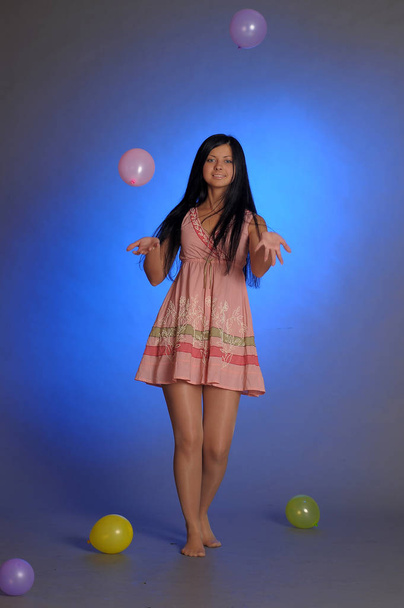 brunette girl in a short pink dress with balloons plays on a blu - Fotografie, Obrázek