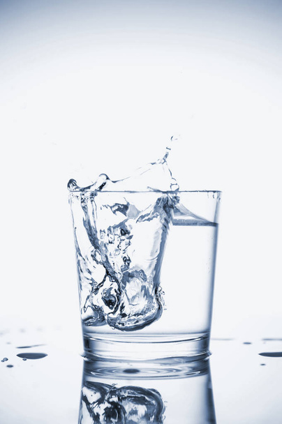 Clear mineral water splashes in a glass with ice. - Photo, Image