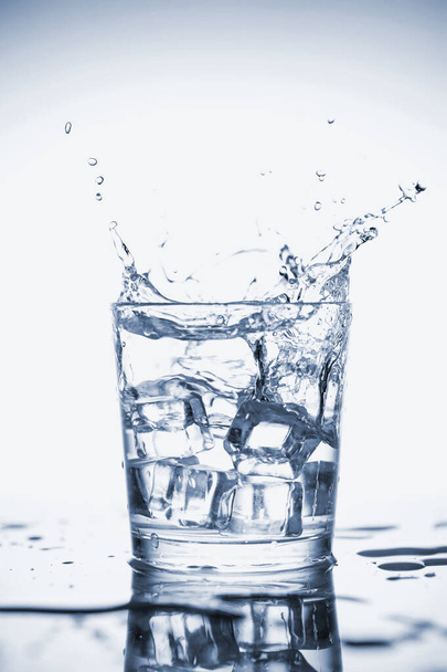 Przezroczysta woda mineralna rozpryskuje się w szklance z lodem. - Zdjęcie, obraz