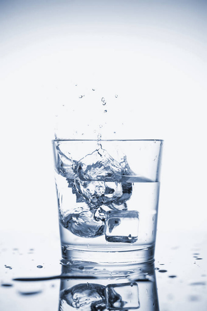 Água mineral transparente espirra em um copo com gelo
. - Foto, Imagem