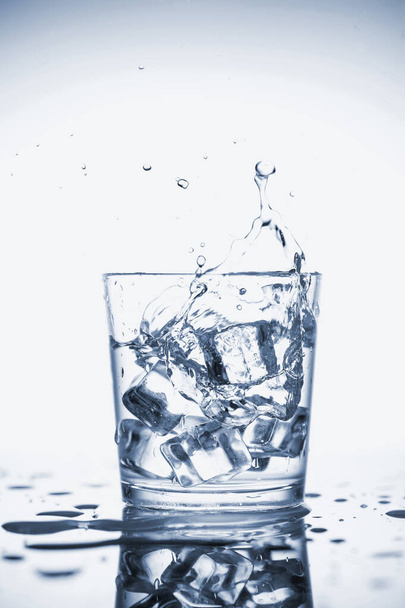 Clear mineral water splashes in a glass with ice. - Photo, image