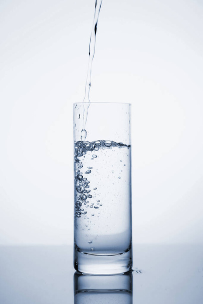 Чистая минеральная вода наливается в стакан со льдом
.  - Фото, изображение