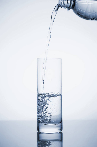 El agua mineral clara se vierte en un vaso con hielo
.  - Foto, Imagen