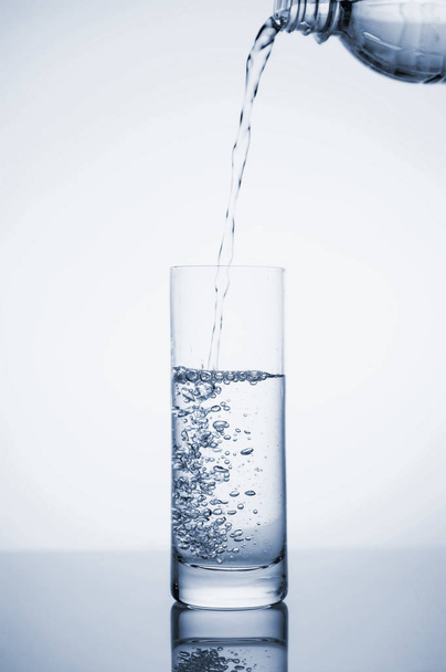 Διαυγές μεταλλικό νερό χύνεται σε ένα ποτήρι με πάγο.  - Φωτογραφία, εικόνα