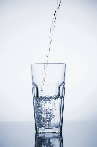 Clear mineral water is poured into a glass with ice.  - 写真・画像