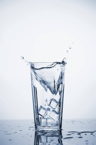 Clear mineral water splashes in a glass with ice. - Foto, Imagen