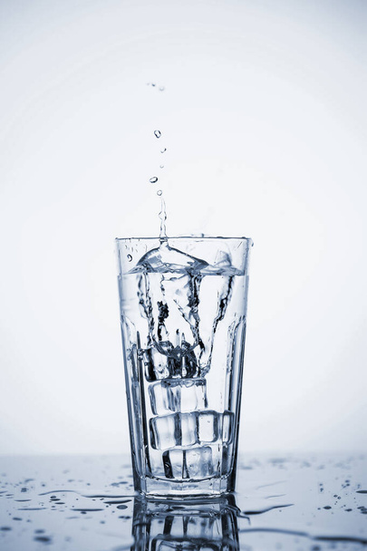 Przezroczysta woda mineralna rozpryskuje się w szklance z lodem. - Zdjęcie, obraz