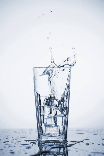 Clear mineral water splashes in a glass with ice. - Photo, Image