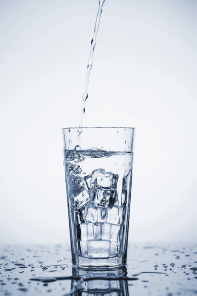 Clear mineral water is poured into a glass with ice.  - Φωτογραφία, εικόνα