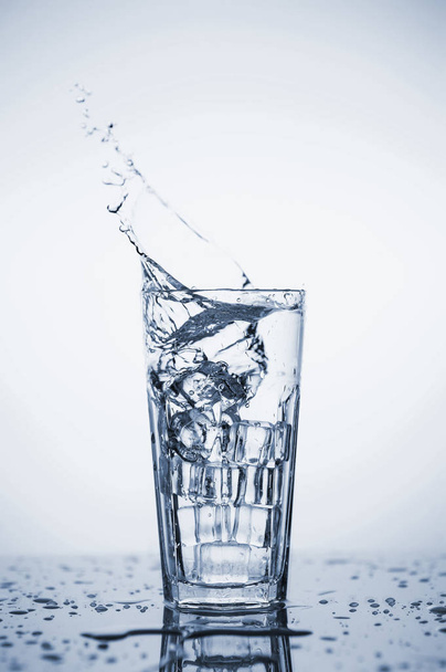 Clear mineral water splashes in a glass with ice. - Zdjęcie, obraz