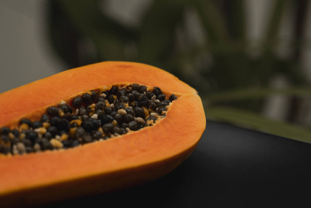 Half of ripe papaya with seed on a black plates and with a green plants on background. Slices of sweet papaya. Halved papayas. Healthy exotic fruits. Vegetarian food. - Fotografie, Obrázek