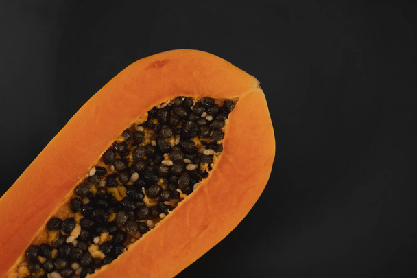 Half of ripe papaya with seed on a black plates and with a green plants on background. Slices of sweet papaya. Halved papayas. Healthy exotic fruits. Vegetarian food. - 写真・画像