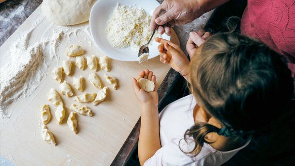 Grandmother with granddaughter is making dumplings with cheese at home kitchen - Фото, изображение