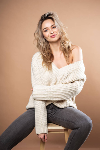 Beautiful blonde woman in a knitted sweater over brown background. Casual style, fashion beauty portrait - Foto, afbeelding