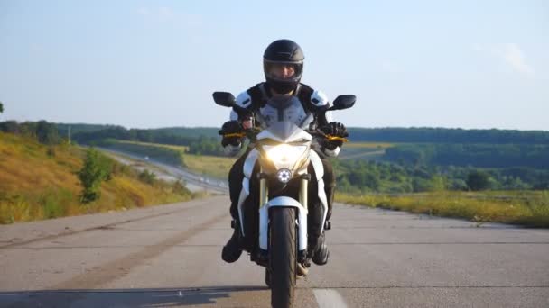 Hombre en casco de conducción poderosa moto deportiva en la carretera con un fondo hermoso. Motociclista exceso de velocidad en motocicleta con faros a lo largo de la carretera del campo. Joven disfrutando de la velocidad. Concepto de libertad - Imágenes, Vídeo