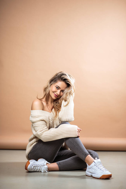 Beautiful blonde woman in a knitted sweater over brown background. Casual style, fashion beauty portrait - Фото, зображення