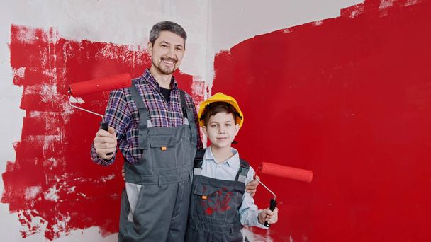 ein Junge und sein lächelnder Vater stehen im Raum und halten Rollen, die mit roter Farbe bedeckt sind - Foto, Bild
