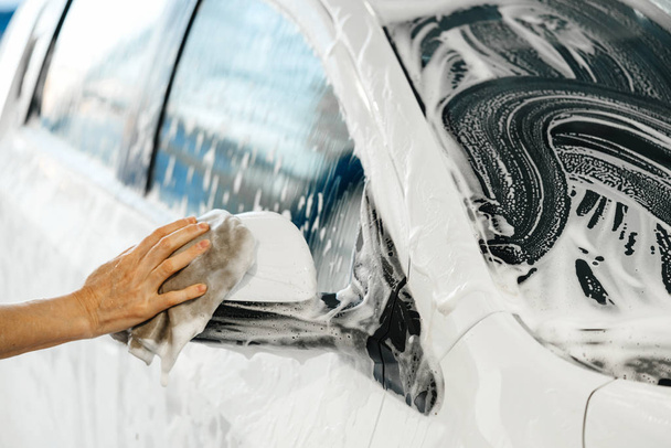 Mulher mão lava um carro branco com uma esponja e espuma em uma lavagem de carro self-service
 - Foto, Imagem