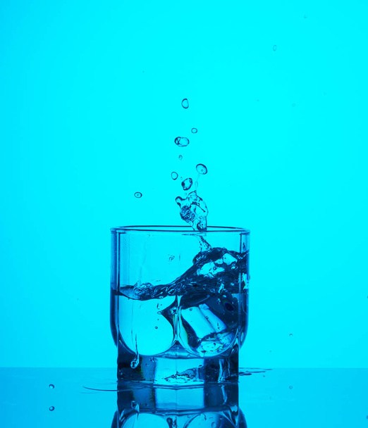 Los cubos de hielo caen en un vaso transparente de agua y crean salpicaduras
 - Foto, Imagen