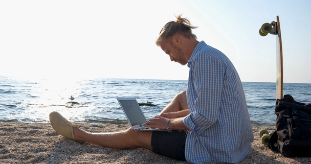 Young handsome male on the summer beach work with laptop during sunrise - Photo, Image