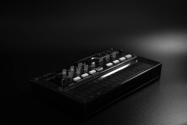 petit synthétiseur analogique de modulation fm, avec boutons et faders, avec effets, arpégiateur et séquenceur, photographie en noir et blanc, sur fond noir
 - Photo, image