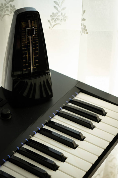 Metronomi auringonvalaistussa pianossa, kopioi ja liitä tilaa, valittu tarkennus, valkoinen verho tausta, musiikkikonsepti
. - Valokuva, kuva