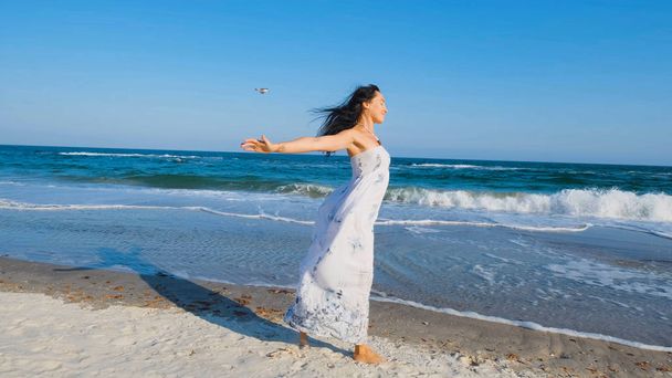 Young beautiful woman dressed in a white dress walk barefoot on the summer beach - Foto, Bild