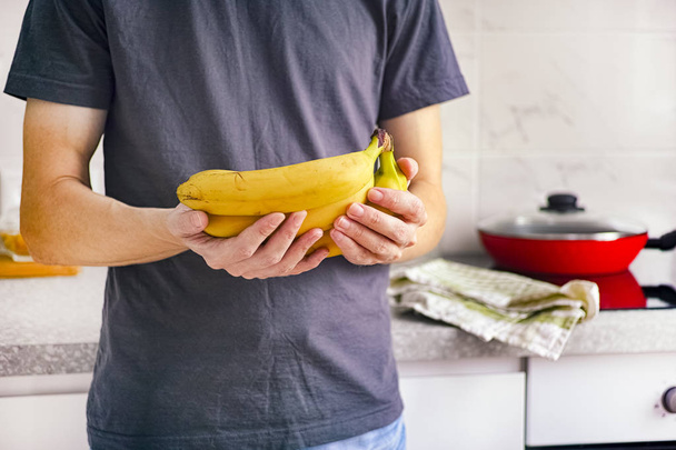 Man die in de keuken staat en bananen in zijn handen houdt - Foto, afbeelding
