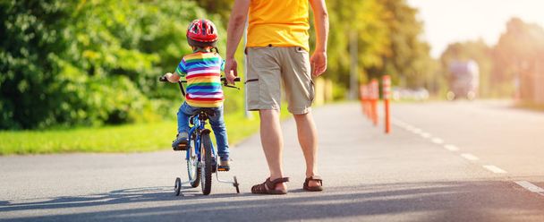 a child on a bicycle in helmet with father on asphalt road - Foto, Imagen