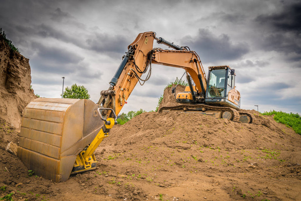 um excavator amarelo está em um monte da terra em um constru grande
 - Foto, Imagem