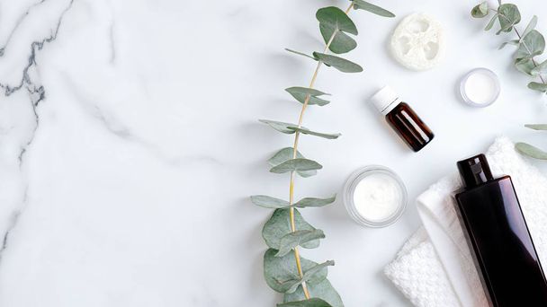 Herbal bodycare cosmetic hygienic cream, lotion, essential oil, towel and eucalyptus leaves. Organic beauty products. Flat lay, top view, copy space. Spa cosmetic products concept - Фото, изображение