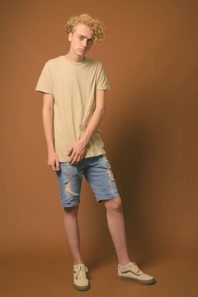 Skinny young man with curly hair against brown background - Fotó, kép