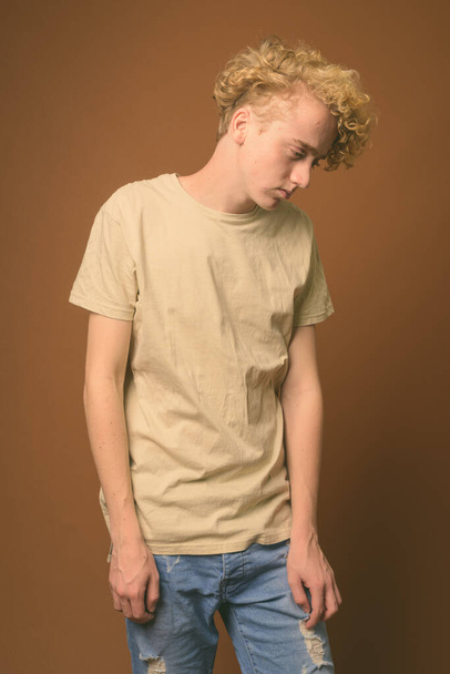 hagerer junger Mann mit lockigem Haar vor braunem Hintergrund - Foto, Bild