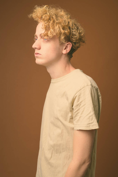 Kahverengi arka plan karşı kıvırcık saçlı sıska genç adam - Fotoğraf, Görsel