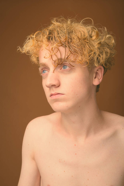 Тощий молодой человек с вьющимися волосами без рубашки на коричневом фоне
 - Фото, изображение