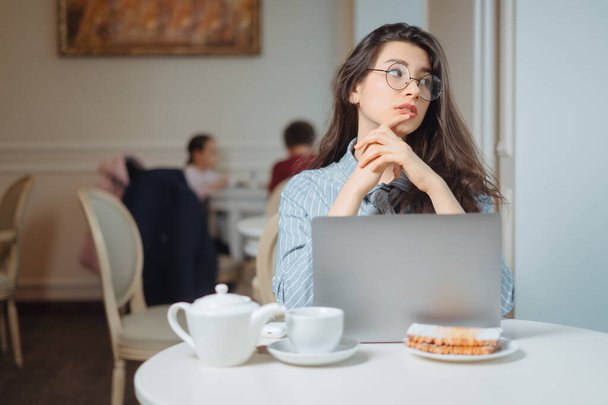 Portrait of a young female freelancer using laptop computer for distance job while sitting in modern coffee shop interior, smart woman working on net-book during morning breakfast in cafe bar - Foto, imagen
