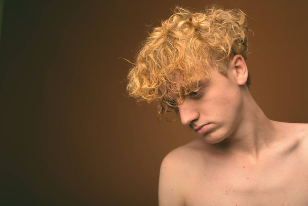 Тощий молодой человек с вьющимися волосами без рубашки на коричневом фоне
 - Фото, изображение