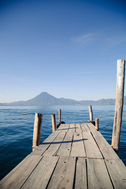 Τοπίο της λίμνης Atitlan στη Γουατεμάλα, αποβάθρα σε μπλε λίμνη που περιβάλλεται από ηφαίστεια και βουνά - βάρκα στη μέση της λίμνης - Φωτογραφία, εικόνα