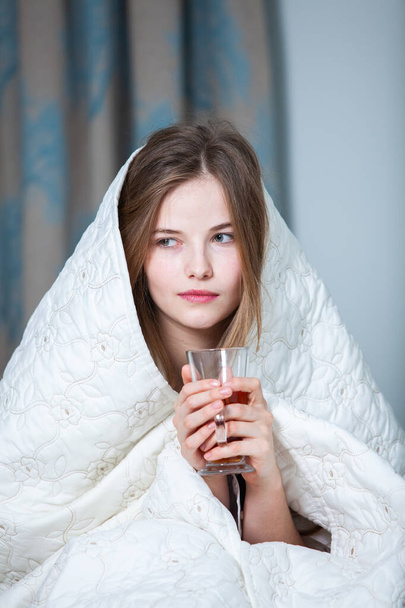 Μια νεαρή όμορφη λευκή γυναίκα ξυπνάει στο φωτεινό δωμάτιο. Χαλαρή γυναίκα ξαπλωμένη στο κρεβάτι και πίνει τσάι. Καλημέρα έννοια. Ρωσίδα.. - Φωτογραφία, εικόνα