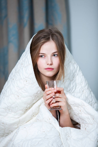 若い美しい白い女性の光の部屋で目を覚ます。ゆったりとした女が寝そべってお茶を飲む。おはようございますロシア人の女の子. - 写真・画像