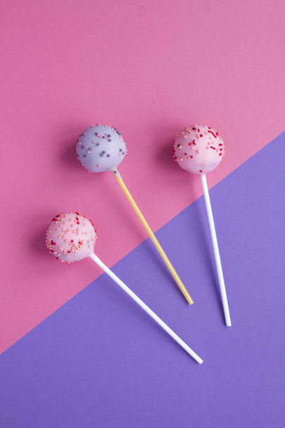 Cake pops with pink and violet glaze  on the two-color background. Top view. Copy space. Location vertical. - Zdjęcie, obraz