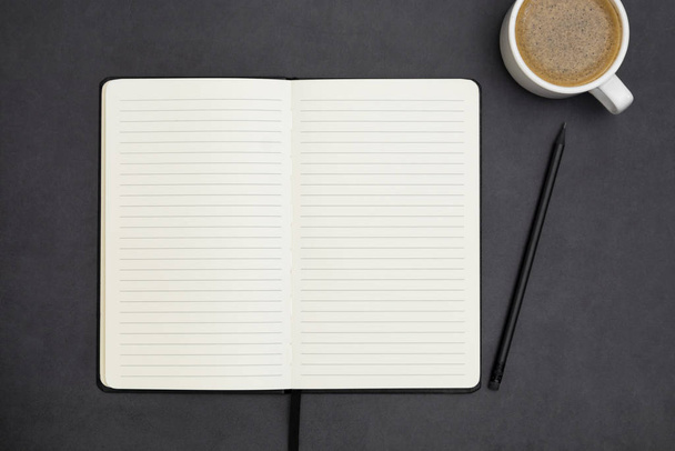 Open notebook with empty page and coffee cup. Table top, work space on dark background. Creative flat lay. - Foto, Bild