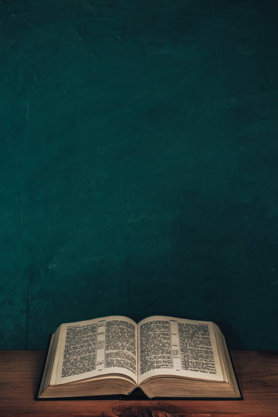 Ανοίξτε τη Βίβλο σε ένα κόκκινο ξύλινο τραπέζι. Όμορφο πράσινο φόντο τοίχο. - Φωτογραφία, εικόνα