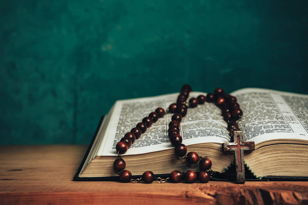 Close up Open Holy Bible and beads crucifix on a red old wooden table. Beautiful green wall background. - Foto, imagen