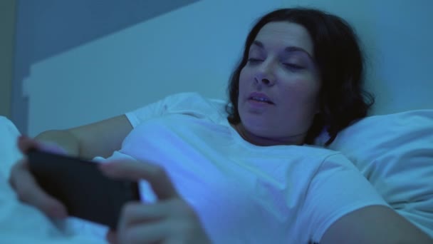 Woman watching video on smartphone in bed, gadget addict sleepless at night - Metraje, vídeo