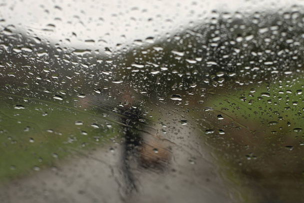 Silhouette d'une femme tenant un panier derrière une goutte de pluie sur une surface en verre de voiture
 - Photo, image