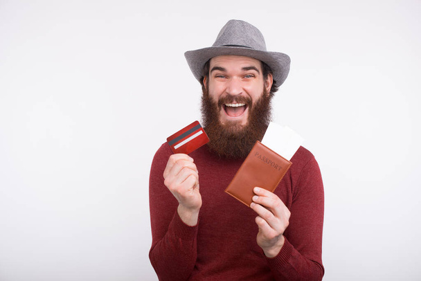 Χαρούμενος γενειοφόρος άνδρας σε casual κρατώντας διαβατήριο με εισιτήρια και πιστωτική κάρτα - Φωτογραφία, εικόνα