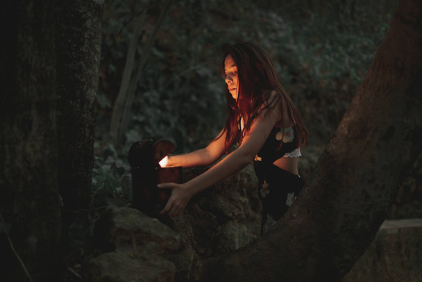 Desde abajo de mujer joven en vestido tomando reloj retro antiguo en caja de madera en piedra en bosque otoñal
 - Foto, Imagen